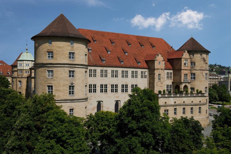 Historisches Schloss mit rotem Dach und grüner Kuppel, umgeben von Bäumen.