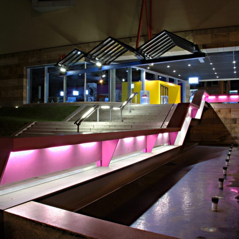 Moderne Außenarchitektur mit farbigen Lichtakzenten und geraden Linien bei Nacht.